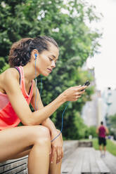 Indian athlete listening to mp3 player in city - BLEF12820