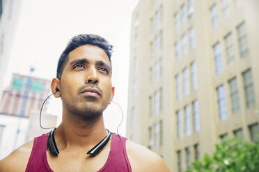 Indian athlete listening to earbuds in city - BLEF12832