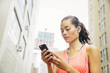 Mixed race athlete listening to mp3 player in city - BLEF12833