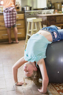 Kaukasisches Mädchen spielt auf einem Gymnastikball in der Küche - BLEF12918