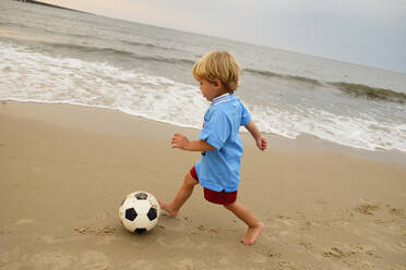 Kaukasischer Junge spielt mit Fußball am Strand - BLEF12935