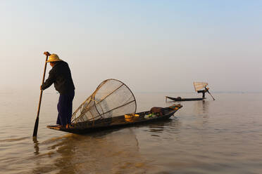 Asiatischer Fischer rudert Kanu auf stillem See - BLEF12948