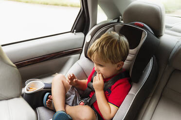 Kaukasischer Junge isst Snack im Autositz - BLEF12962