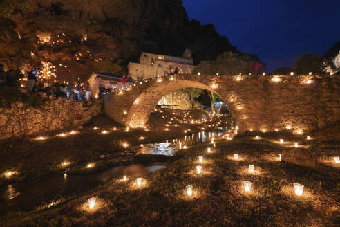 Medieval bridge over river surrounded by lit candles in town at night, Burgos Province, Spain - DHCF00197