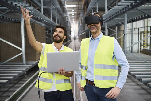 Mann mit Laptop und Geschäftsmann mit VR-Brille in einer Fabrik - BSZF01183