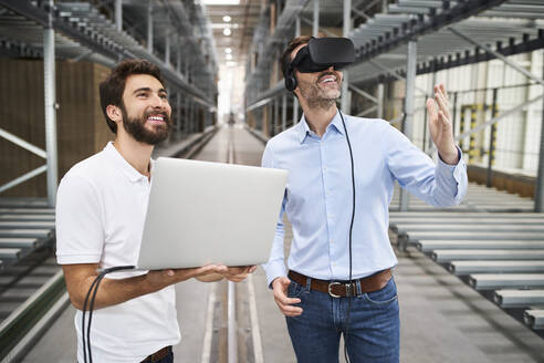 Mann mit Laptop und Geschäftsmann mit VR-Brille in einer Fabrik - BSZF01185