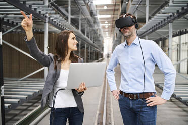 Geschäftsfrau mit Laptop und Geschäftsmann mit VR-Brille in einer Fabrik - BSZF01188