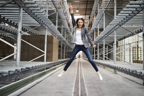 Excited businesswoman jumping in factory - BSZF01208