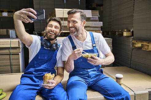 Zwei glückliche Arbeiter machen Mittagspause und machen ein Selfie in einer Fabrik - BSZF01217
