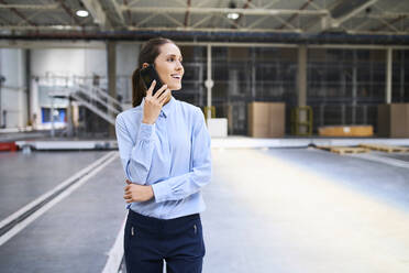 Lächelnde Geschäftsfrau am Mobiltelefon in einer Fabrik - BSZF01225