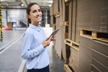 Portrait of smiling businesswoman with tablet in a factory warehouse - BSZF01234