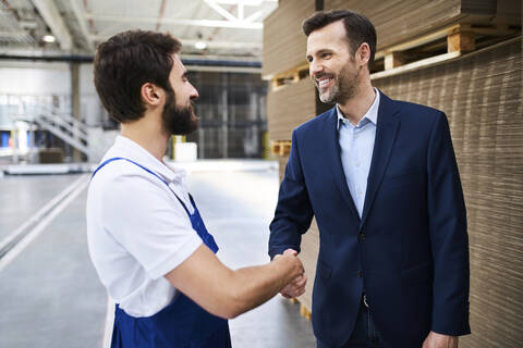 Geschäftsmann und Arbeiter schütteln sich die Hände in einer Fabrik, lizenzfreies Stockfoto