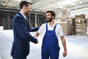 Geschäftsmann und Arbeiter schütteln sich die Hände in einer Fabrik - BSZF01242