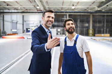 Glücklicher Geschäftsmann und Arbeiter in einer Fabrik - BSZF01245