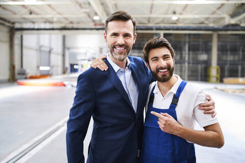 Porträt eines glücklichen Geschäftsmannes und eines Arbeiters in einer Fabrik, lizenzfreies Stockfoto