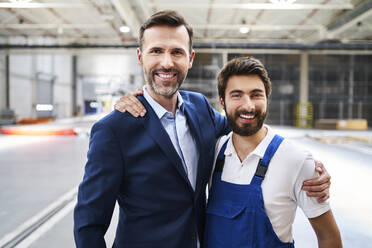 Porträt eines glücklichen Geschäftsmannes und eines Arbeiters in einer Fabrik - BSZF01253