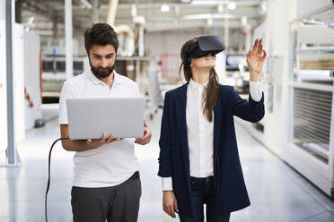 Mann mit Laptop und Geschäftsfrau mit VR-Brille in einer Fabrik - BSZF01278