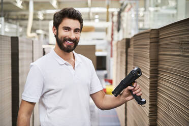 Portrait of smiling man in factory hall with barcode scanner - BSZF01279