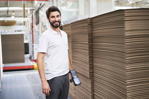 Porträt eines lächelnden Mannes in einer Fabrikhalle mit Barcode-Scanner, lizenzfreies Stockfoto