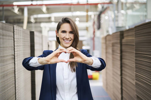 Portrait of happy businesswoman in factory warehouse shaping a heart with her hands stock photo