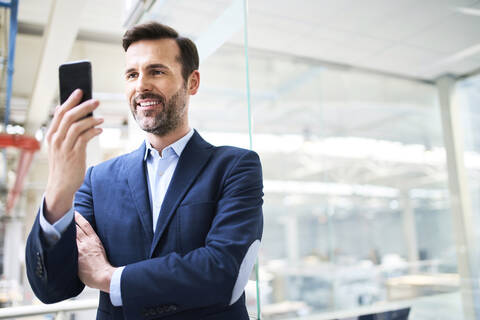 Smiling businessman using cell phone in factory stock photo