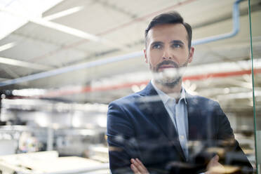 Portrait of a businessman behind glass pane in a factory - BSZF01301