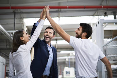 Happy businessman and employees high fiving in a factory - BSZF01311