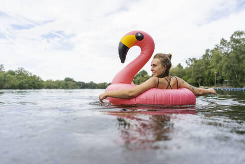 Young woman floating on a lake in a pink flamingo floating tire - GUSF02280