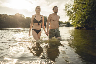 Young couple walking out of lake, holding hands - GUSF02307