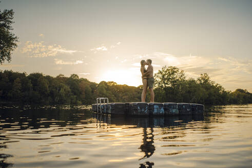 Young couple standing on bathing platform on a lake, embracing - GUSF02315