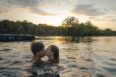 Young couple swimming in lake, kissing at sunset - GUSF02323