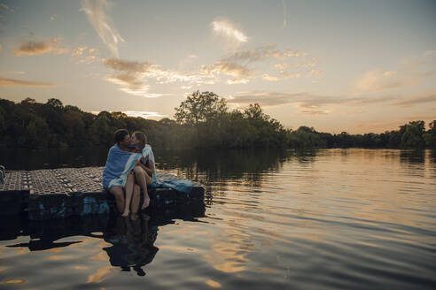 Young couple sitting on bathing platform, kissing, wrapped in towel - GUSF02360