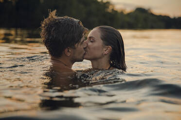 Young couple swimming in lake, kissing at sunset - GUSF02361