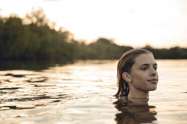 Young woman swimming in lake at sunset - GUSF02362