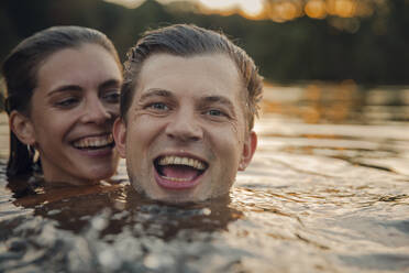 Young couple swimming in lake at sunset - GUSF02365