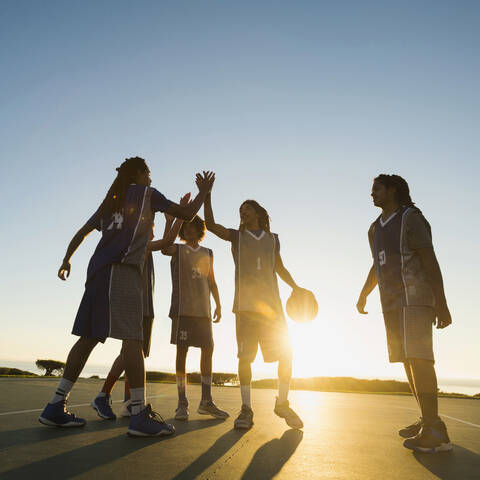 Back lit basketball team high fiving on court stock photo