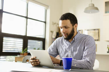 Mixed race businessman using tablet computer at desk - BLEF13042