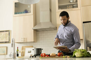 Mixed race man cooking with tablet computer in kitchen - BLEF13047