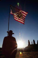 Mann hält die Flagge der Vereinigten Staaten mit einer Darstellung der amerikanischen Ureinwohner in der Nähe von Felsformationen, Monument Valley, Utah, Vereinigte Staaten - BLEF13099