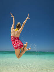 Caucasian woman jumping for joy in tropical ocean - BLEF13114