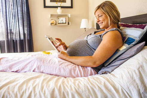 Schwangere kaukasische Frau mit digitalem Tablet im Bett - BLEF13147