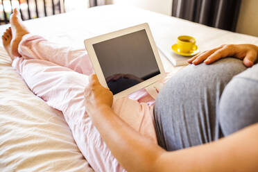 Schwangere kaukasische Frau mit digitalem Tablet im Bett - BLEF13148