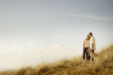 Caucasian couple walking dog on grassy dunes - BLEF13163