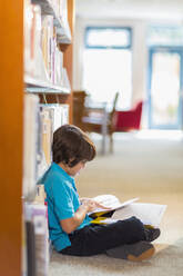 Gemischtrassiger Student liest Bücher auf dem Boden in der Bibliothek - BLEF13289