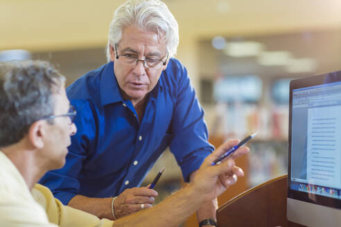 Teacher helping adult student use computer in library - BLEF13296