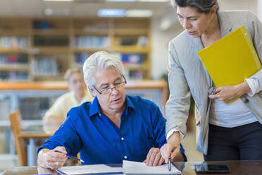 Lehrerin hilft erwachsenem Schüler in der Bibliothek - BLEF13313