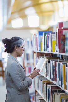 Ältere hispanische Frau liest ein Buch in der Bibliothek - BLEF13329