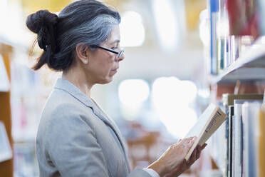 Ältere hispanische Frau liest ein Buch in der Bibliothek - BLEF13330