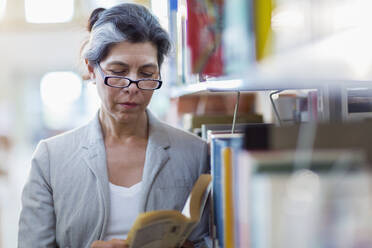 Older Hispanic woman reading book in library - BLEF13331
