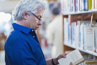 Älterer hispanischer Mann liest ein Buch in einer Bibliothek - BLEF13332
